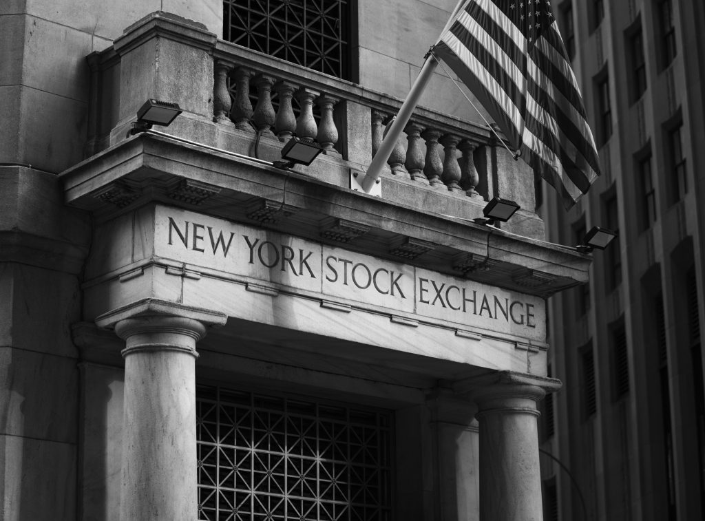 Black and white photo of the New York Stock Exchange facade with USA flag.