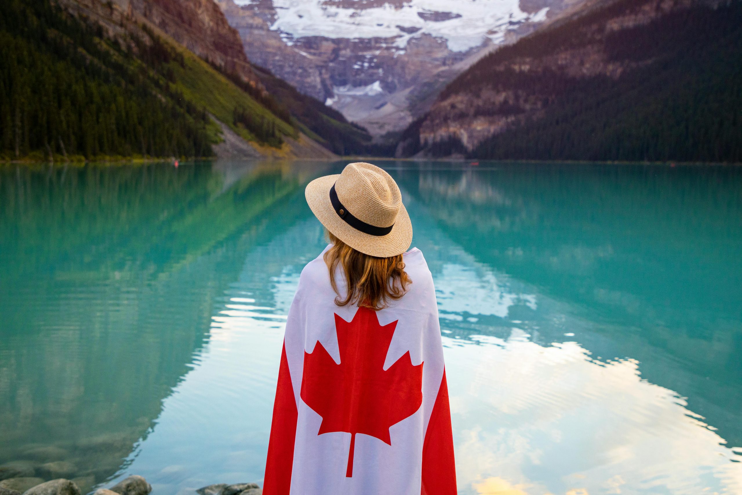 Woman in sun hat with Canadian flag enjoying tranquil Lake Louise, Alberta.