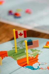 Close-up of miniature Canada and USA flags on a world map depicting North America, symbolizing travel and education.